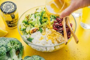 Pouring honey mustard dressing into broccoli salad