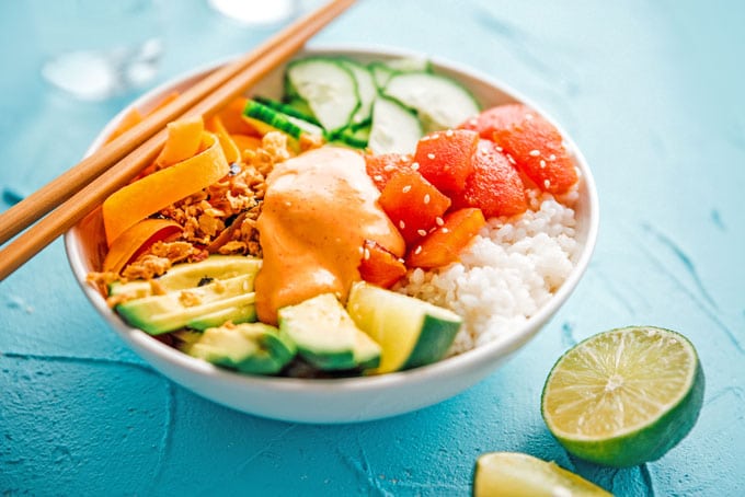 Vegan tomato tuna sushi bowl with rice, avocado, and cucumber in a bowl on a blue background