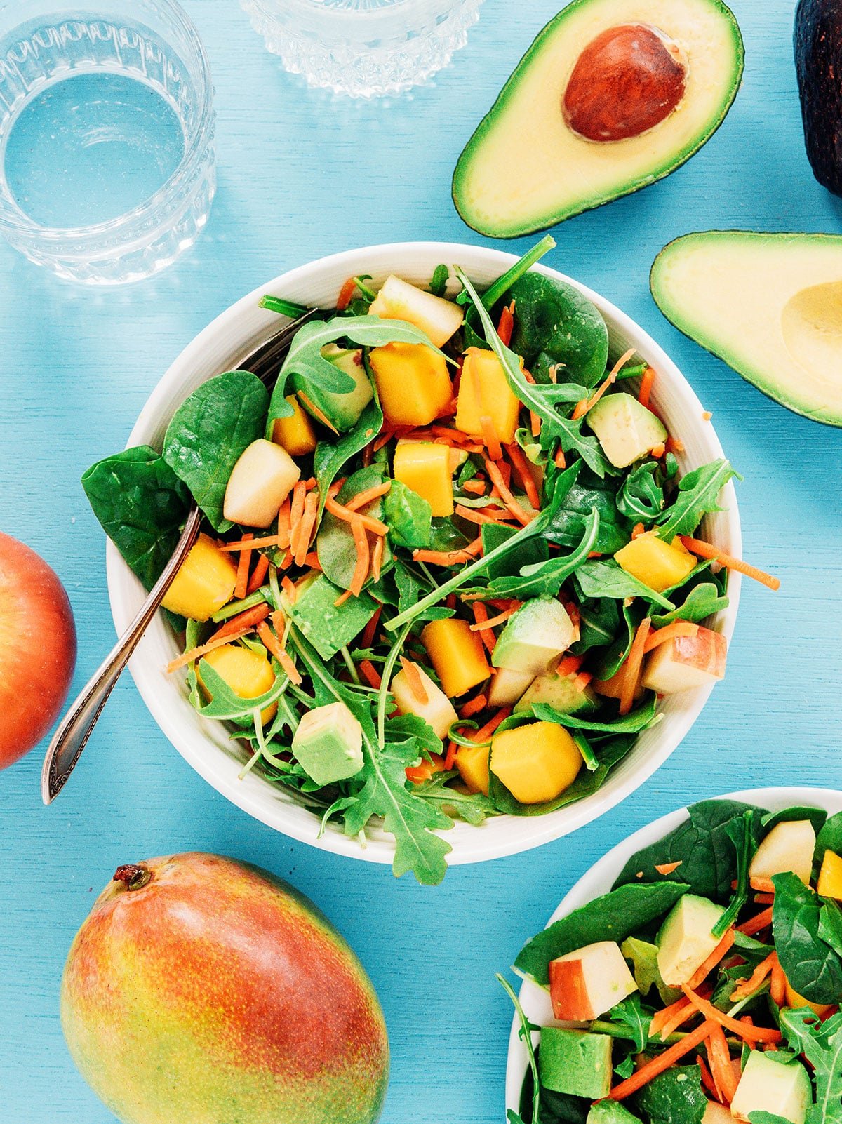 Salad with avocado and mangoes in a white bowl on a blue table