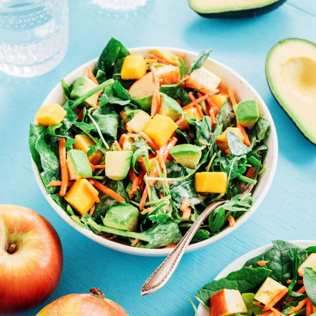 Salad with avocado and mangoes in a white bowl on a blue table