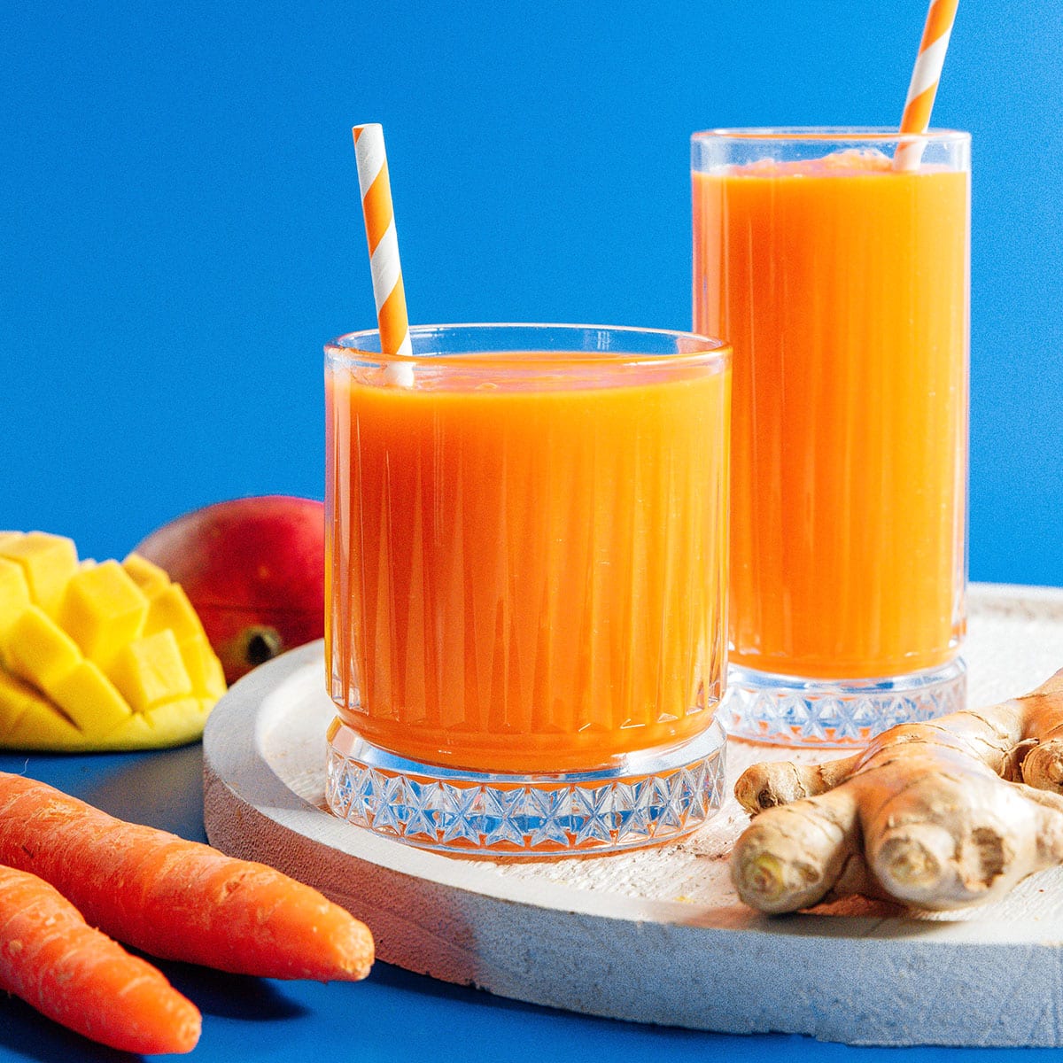 Carrot juice in two classes with ginger and mango nearby.
