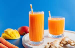 Carrot juice in two classes with ginger and mango nearby.