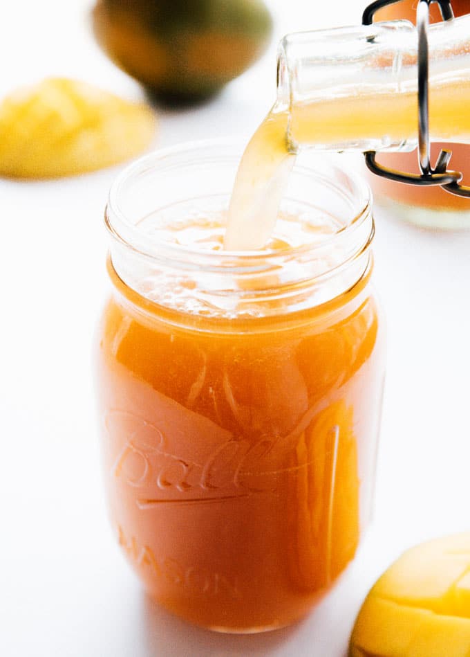 Pouring homemade mango kombucha into a mason jar