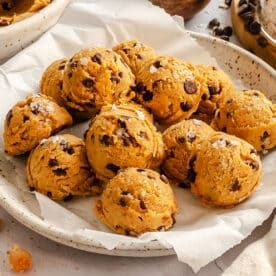 A plate with scoops of chocolate chip cookie dough dessert hummus, arranged on parchment paper, surrounded by oats, chickpeas, and chocolate chips.