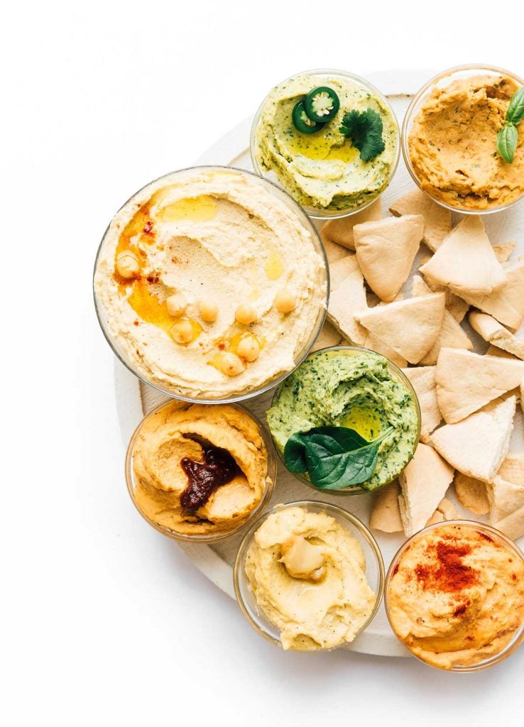 Rainbow variety of hummus in bowls on a white background