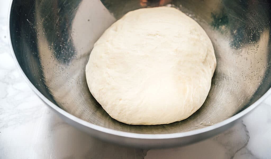 Kneaded pizza dough before rise on a marble background.