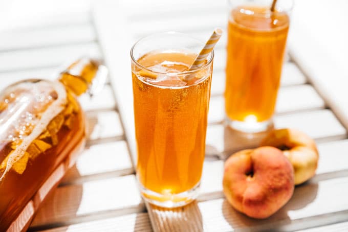 Fizzy peach kombucha in a glass with paper straw