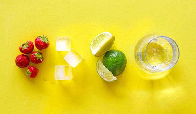Ingredients to make strawberry limeade on a yellow background