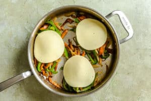 A skillet with sautéed onions, green peppers, and mushrooms topped with three slices of provolone cheese for a savory vegetarian Philly cheesesteak experience.