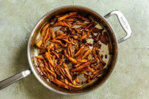 A stainless steel pan containing cooked, sliced mushrooms—perfect for a vegetarian Philly cheesesteak—sits on a textured gray surface.