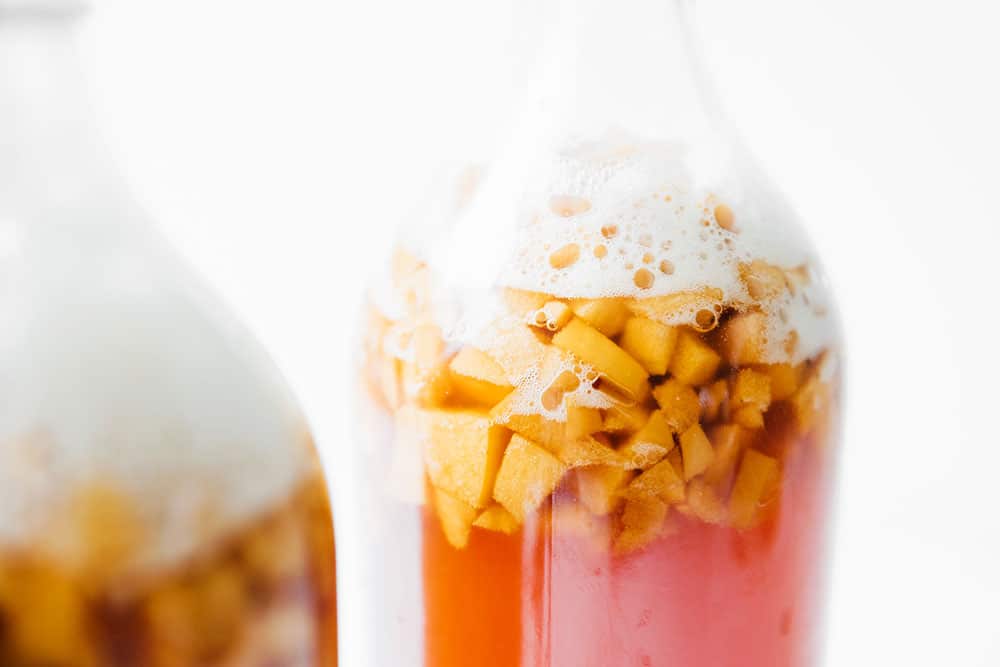 Closeup photo of apple kombucha in fermentation bottles on a white background
