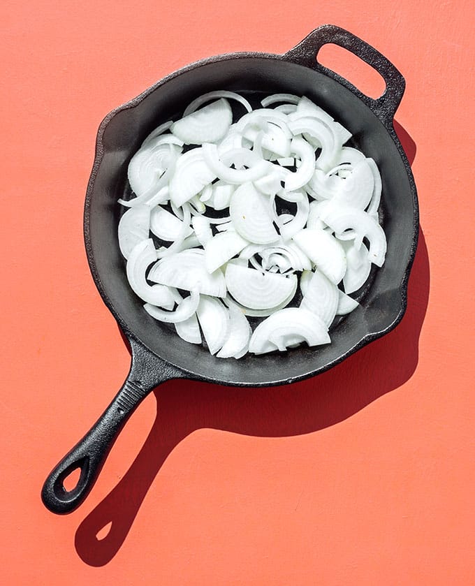 Onions in a cast iron skillet on pink background