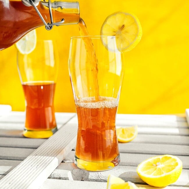 Pouring kombucha into a glass with a yellow background