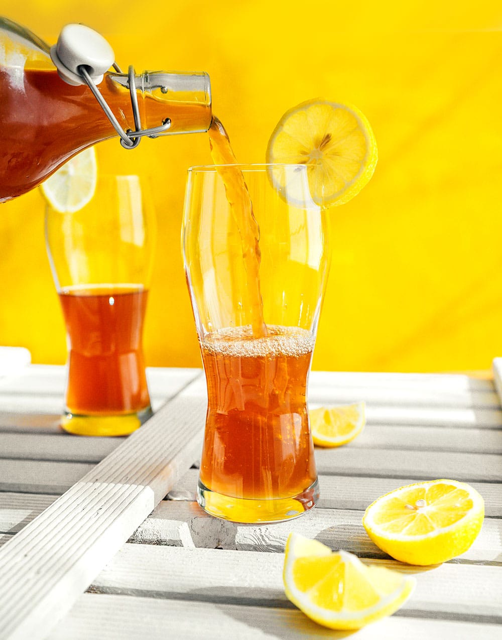 Pouring kombucha into a glass with a yellow background