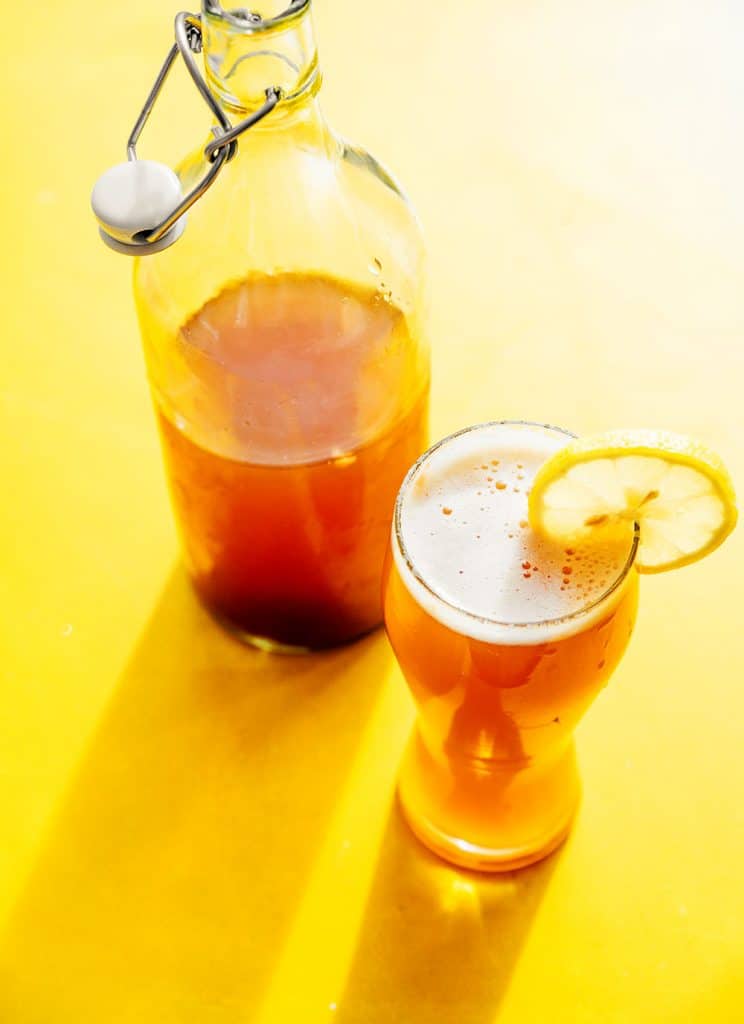 Kombucha shandy in a glass with a lemon on a yellow background