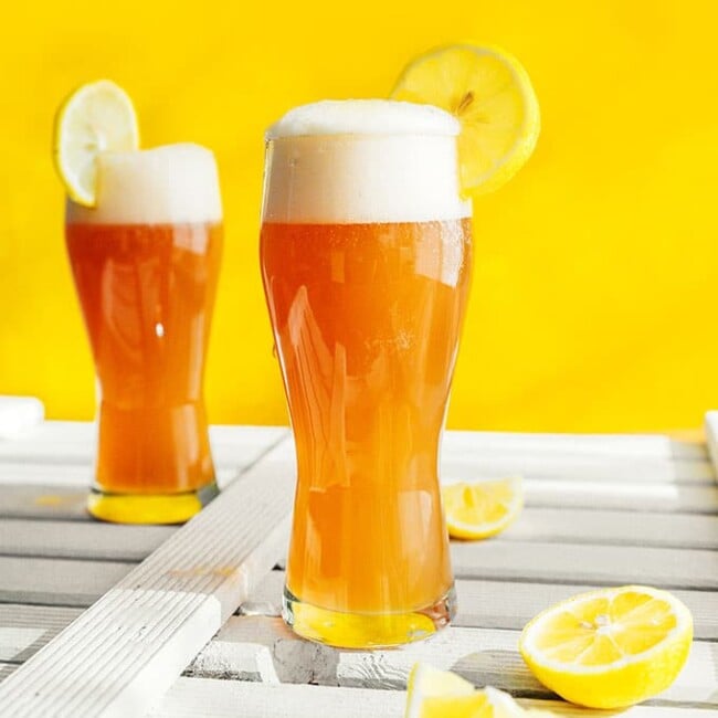 Kombucha shandy in a glass with a lemon on a yellow background