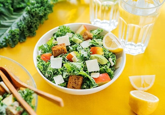 Kale salad with apples and avocado in a bowl on a yellow background