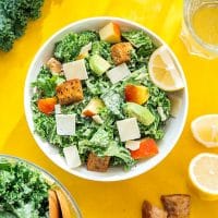 Kale salad with apples and avocado in a bowl on a yellow background