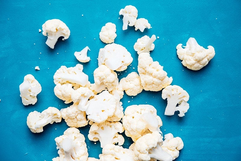 Uncooked cauliflower florets sprinkled across a blue background