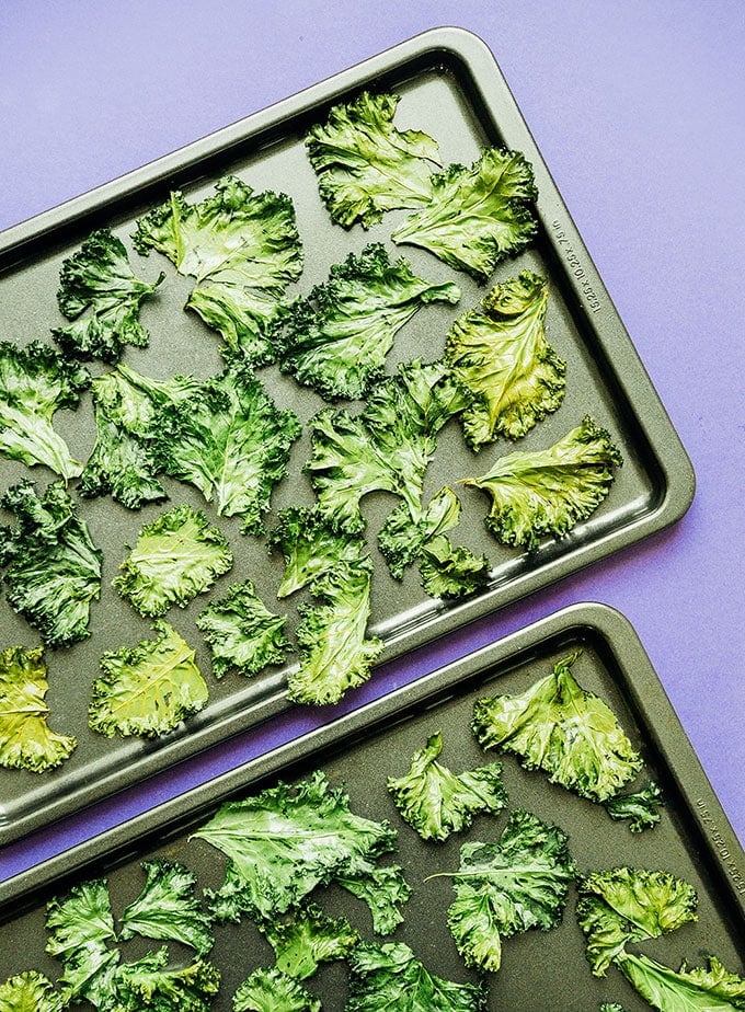 Baking sheet of kale chips on a purple background