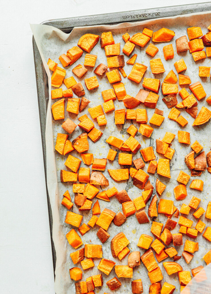 A baking sheet lined with parchment paper and covered with a single layer of diced sweet potato