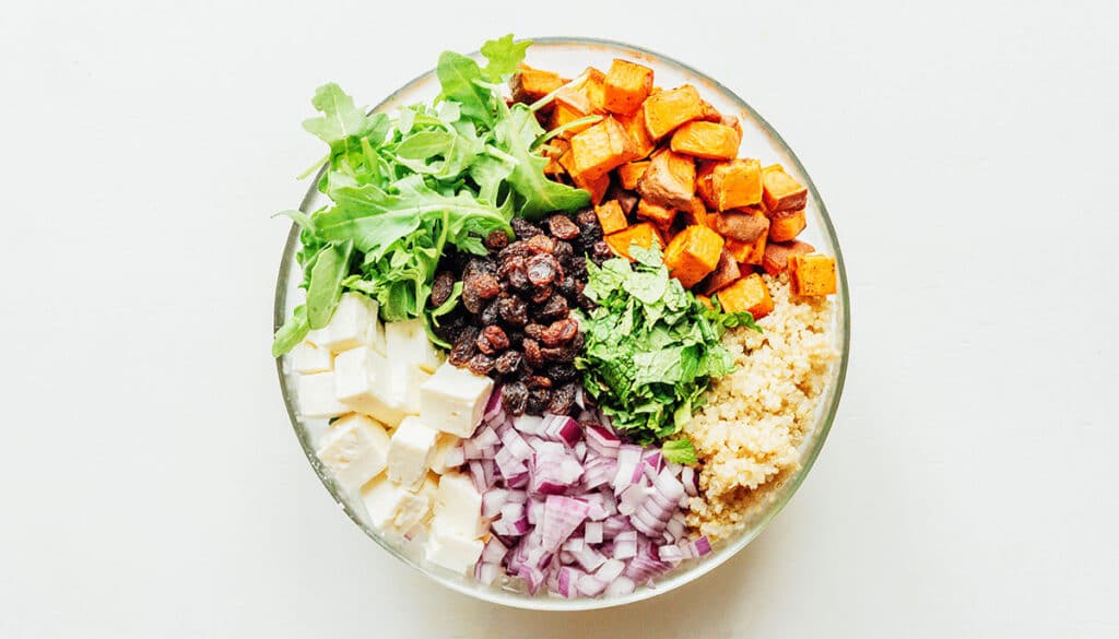 A clear glass bowl filled with sweet potato salad ingredients
