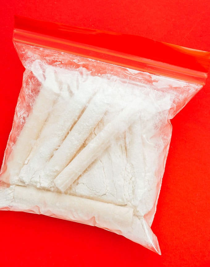 Mozzarella sticks in a plastic bag of flour on a red background