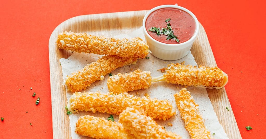 Mozzarella sticks and marinara sauce on a wooden plate on a red background
