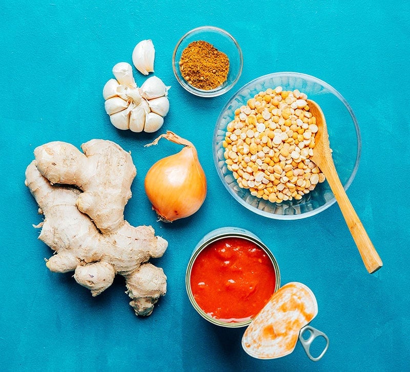 Garlic, ginger, onion, chana dal, diced tomatoes, and spices on a blue background