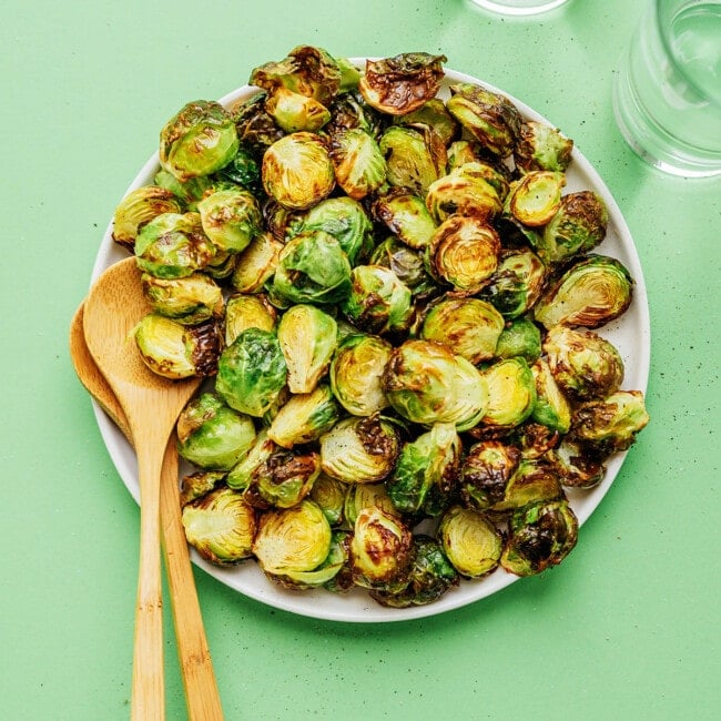Brussels sprouts on a plate with wooden serving spoons.