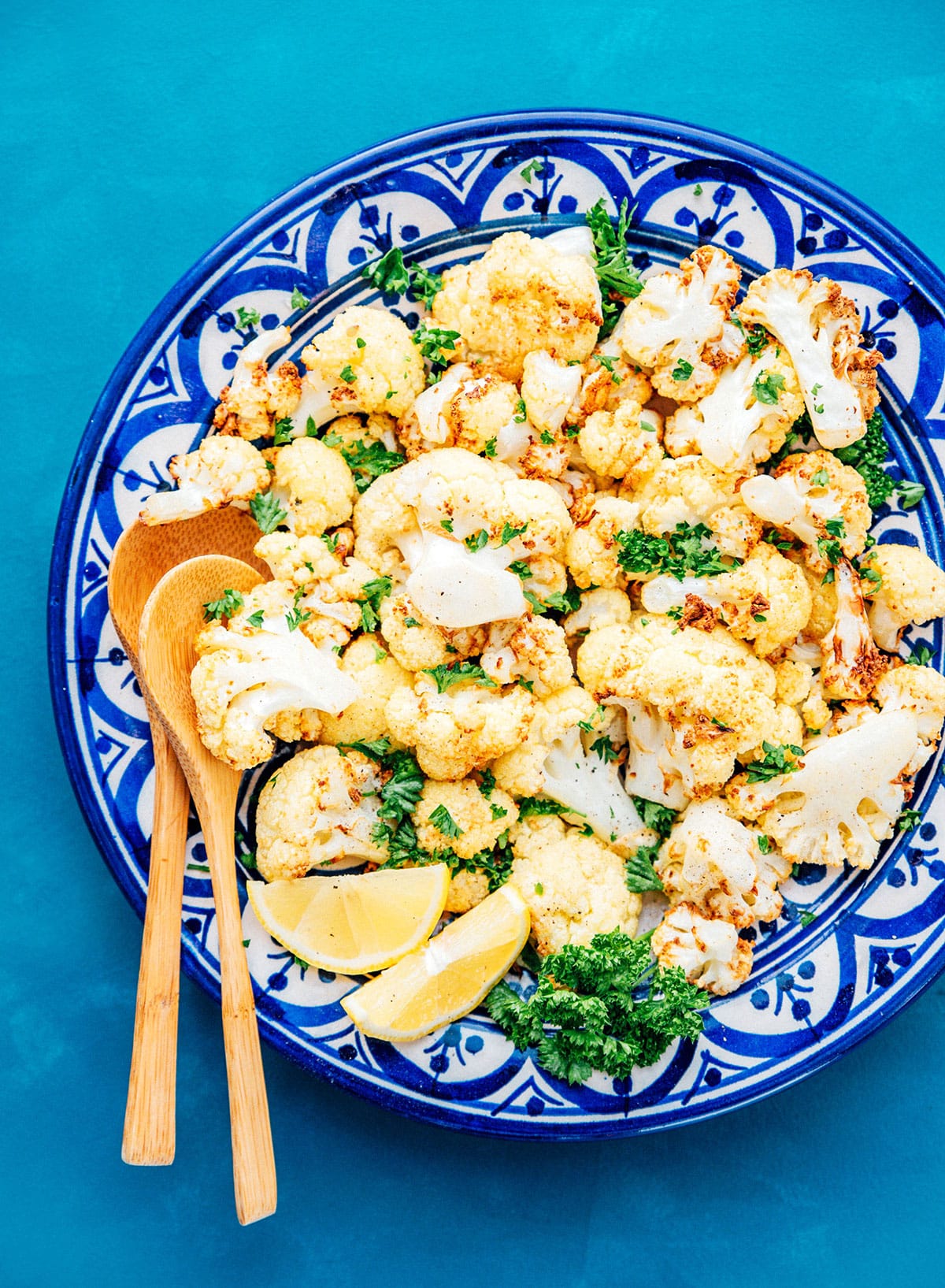 Air fryer cauliflower on a blue plate with wooden spoons.