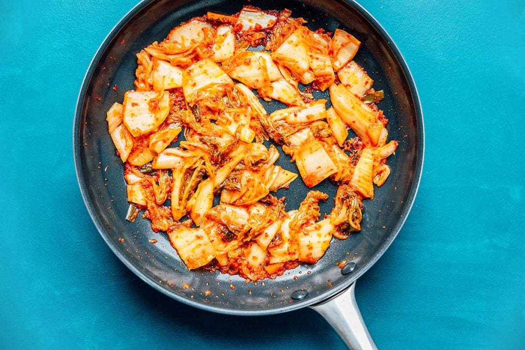 Kimchi being sautéed in a sauce pan on a blue background
