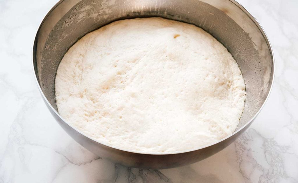Risen naan dough in a bowl on a white background