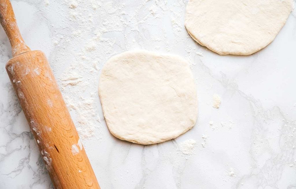 Naan dough slices flattened into flatbreads on a white background