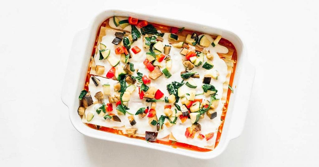 A casserole dish filled with marinara, mozzarella, lasagna noodles, bechamel, and vegetables