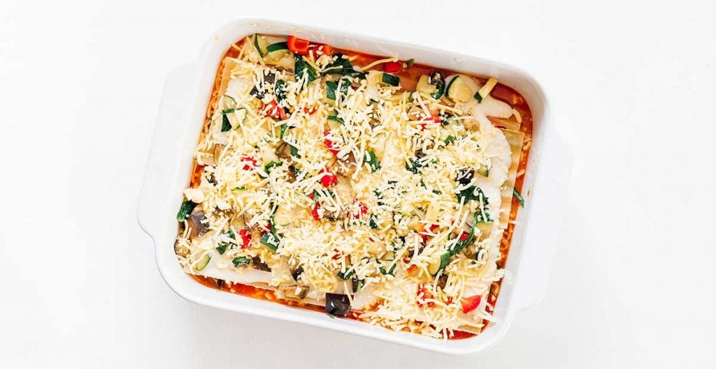 A casserole dish filled with marinara, lasagna noodles, bechamel, veggies, and mozzarella