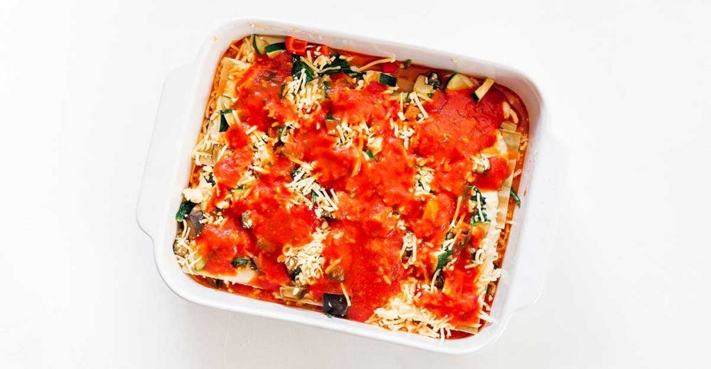A casserole dish filled with lasagna noodles, bechamel, veggies, mozzarella, and marinara