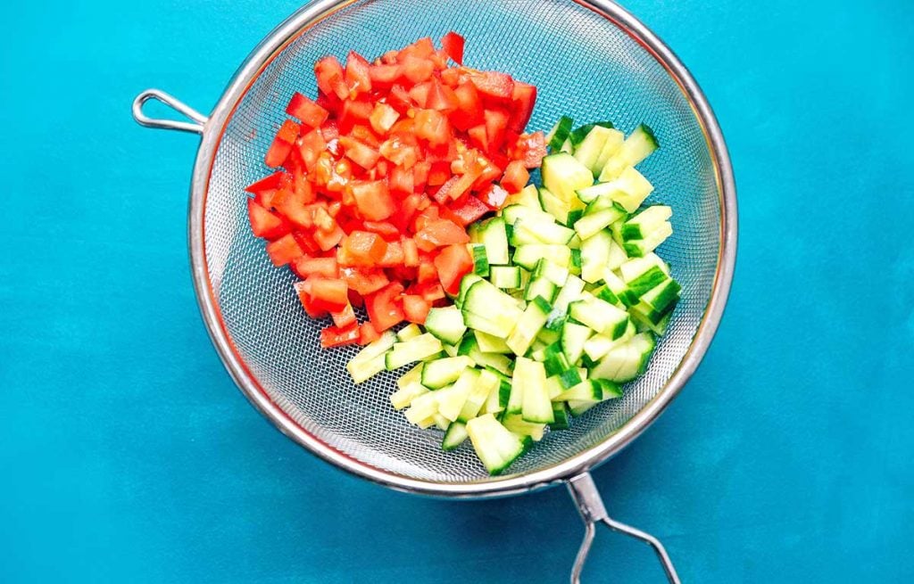 Chopped tomato and cucumber in a colander on a blue background