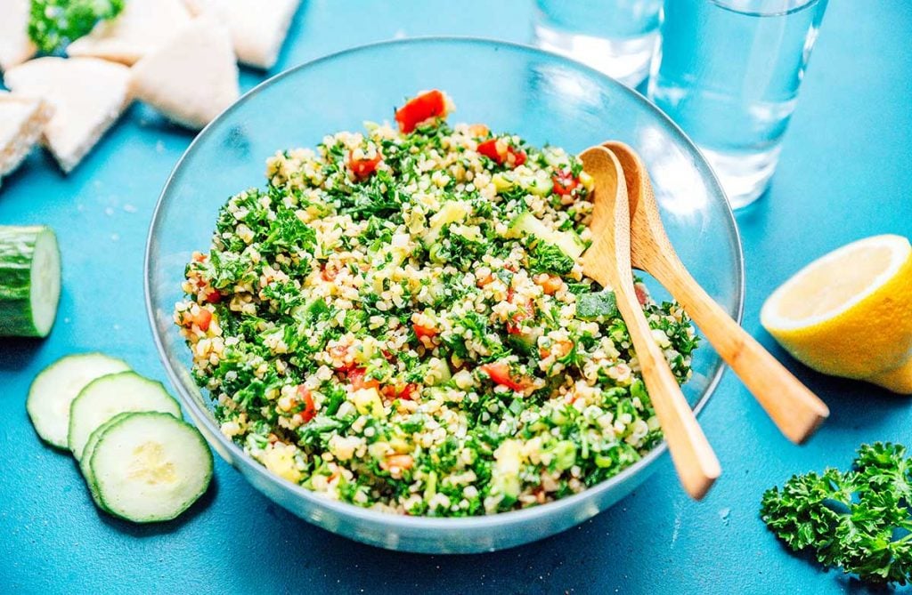 Clear bowl of tabbouleh with other Mediterranean meal prep ingredients lying around