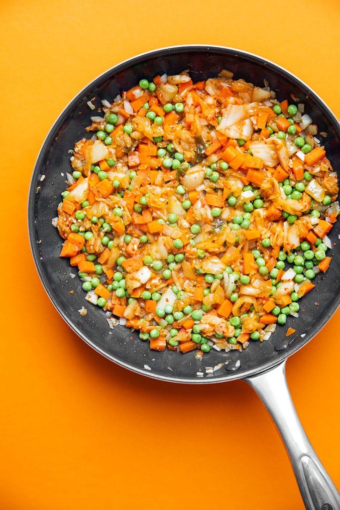 Vegetables and kimchi cooking in a skillet on an orange background