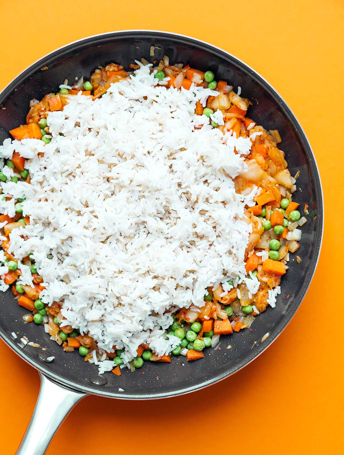 Vegetables, kimchi, and rice cooking in a skillet on an orange background