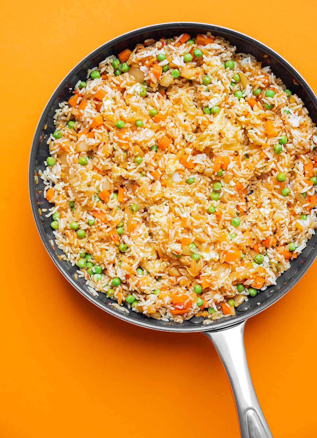 Kimchi fried rice cooking in a skillet on an orange background