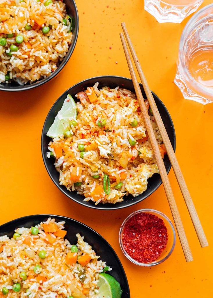Three bowls of kimchi fried rice on an orange background