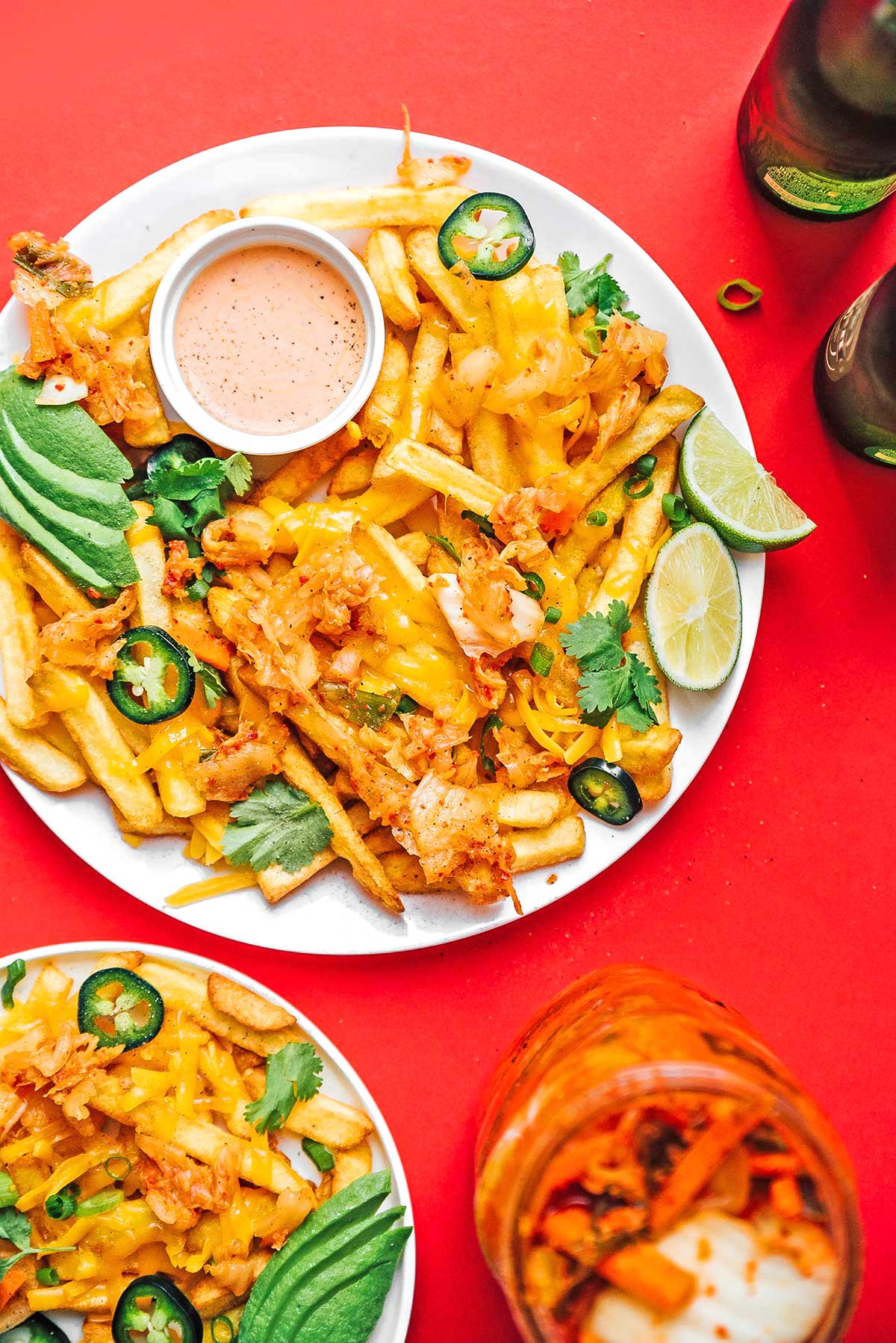 Kimchi fries, sauce, avocado slices, lime slices, and toppings on a plate on a red background