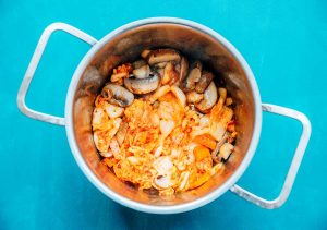 A pot of cooked mushrooms and onions sits invitingly on a blue surface, hinting at the promise of a delicious kimchi ramen twist.
