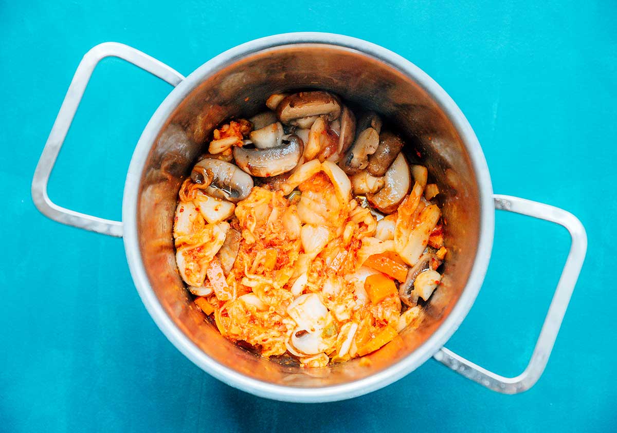 Kimchi and button mushrooms cooking in a pot on a blue background