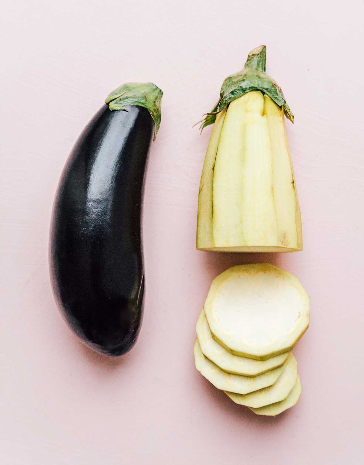 One full eggplant lying beside one peeled, sliced eggplant