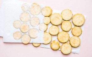 Sliced zucchini rounds rest on paper towels to absorb moisture, perfect for pairing with a creamy serving of baba ganoush.