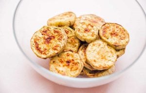 A glass bowl brimming with round, golden-brown roasted eggplant slices, the perfect base for a delightful baba ganoush.