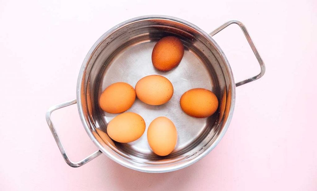 Six eggs in a pot filled with water on a pink background